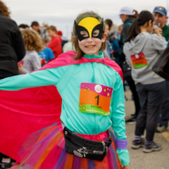Smiling Girls on the Run participant smiles before running the 5K, wearing her cape, tutu, and superhero mask!
